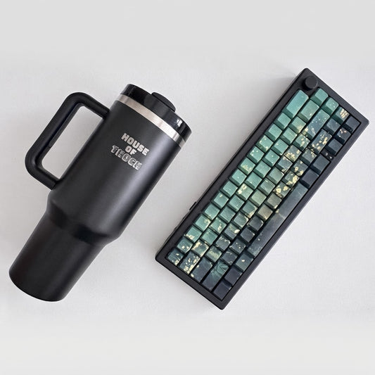 Green Envy keyboard with green and gold keycaps in a pitch-black frame next to an ink House of Thock tumbler