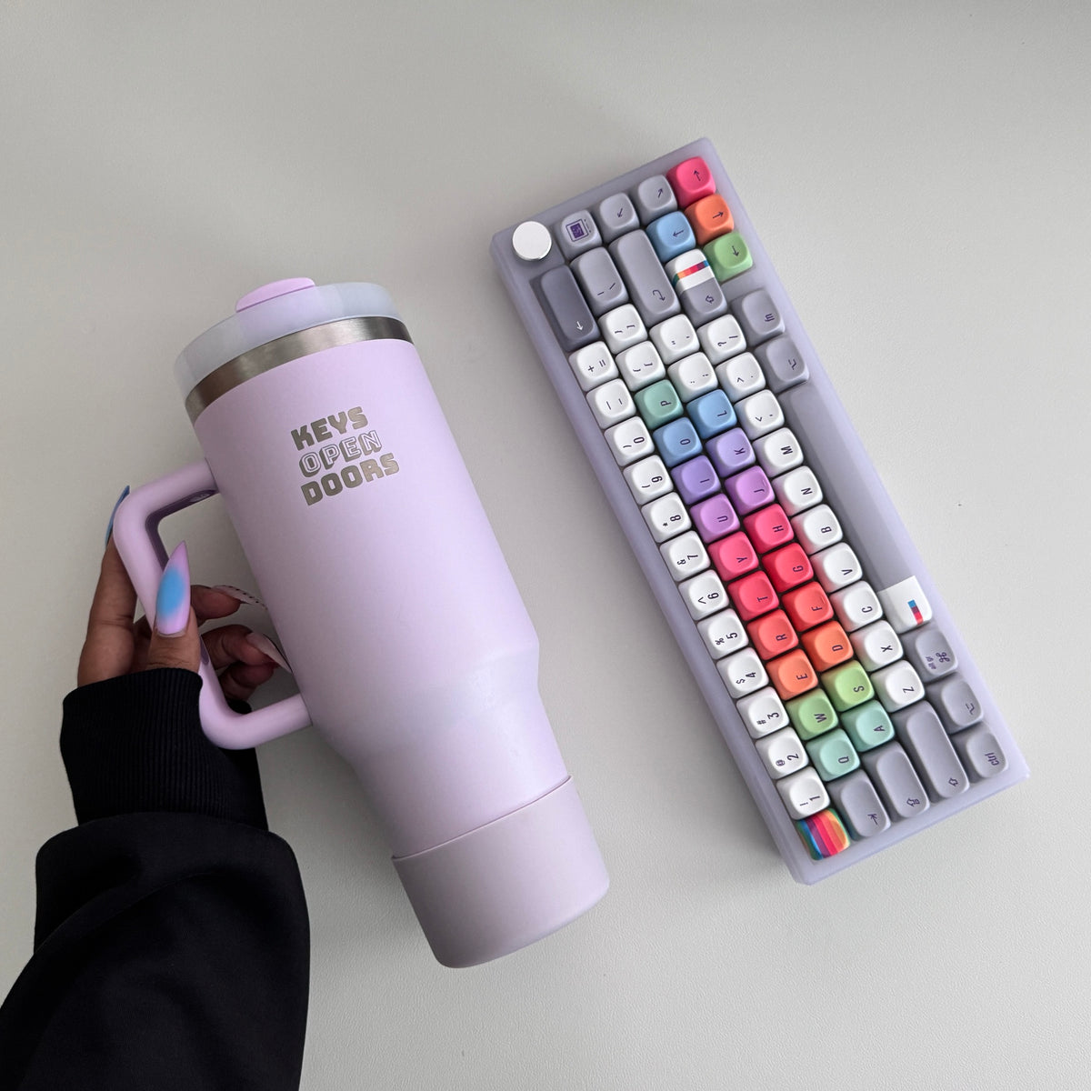 Hand with long nails holding the lilac Keys Open Doors tumbler next to the translucent purple Frost keyboard